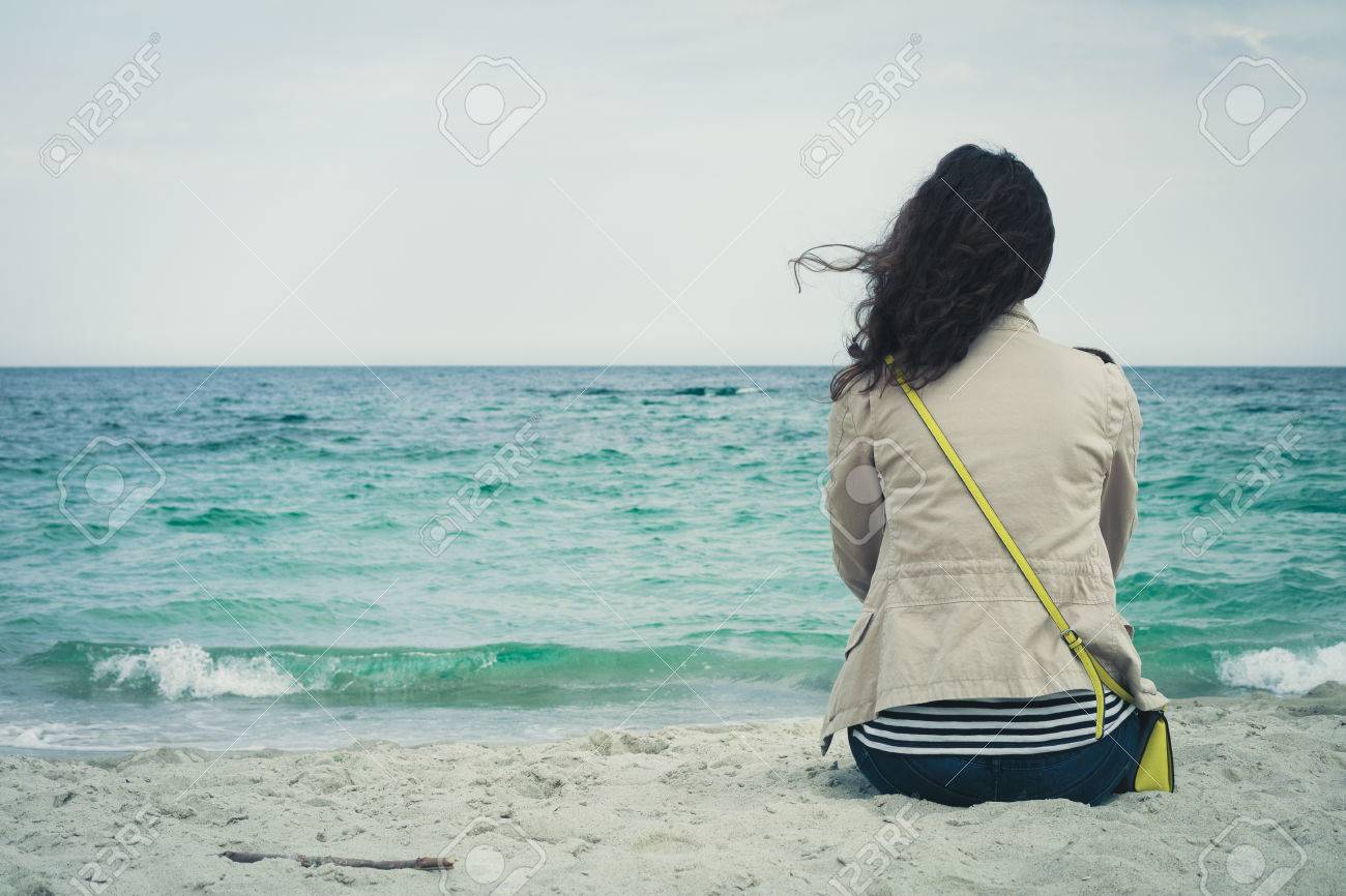 Young cute girl with curly hair sitting on an empty beach